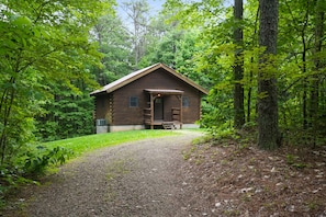 A rustic cabin with a wooden exterior, a front porch, and a gravel path leading to it.