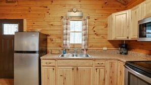 Una cocina con armarios de madera, un refrigerador de acero inoxidable, un microondas y una ventana con cortinas.