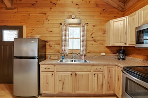 A kitchen with wooden cabinets, a stainless steel refrigerator, a microwave, and a window with curtains.
