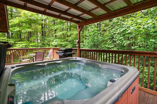 A hot tub on a wooden deck with a view of a forest.