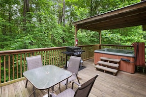 A wooden deck with a glass table and chairs, a barbecue grill, and a hot tub.
