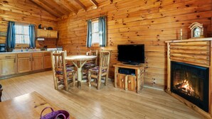 A log cabin interior with a dining area, kitchen, and fireplace. - Sunset Ridge Cabin | 200 Acres, Pets, Hot Tub (South Bloomingville)