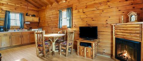 A log cabin interior with a dining area, kitchen, and fireplace.