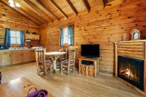 A wooden cabin interior with a dining area, kitchen, and fireplace. - Sunset Ridge Cabin | 200 Acres, Pets, Hot Tub (South Bloomingville)