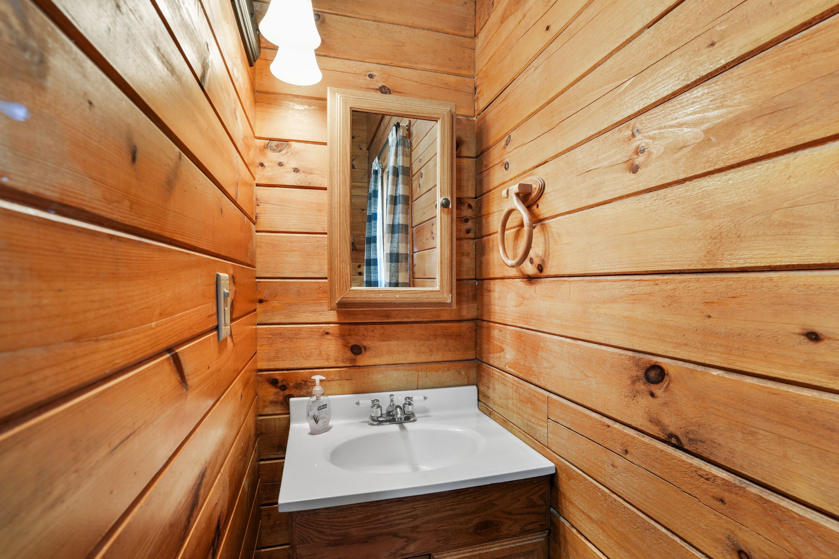 Un baño de cabaña de madera con un lavabo blanco, un espejo y una ventana.