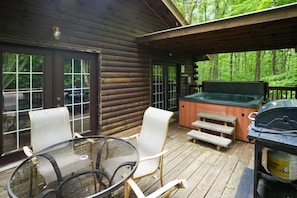 A wooden cabin with a glass table and chairs, a hot tub, and a grill on the deck. - Sunset Ridge Cabin | 200 Acres, Pets, Hot Tub (South Bloomingville)