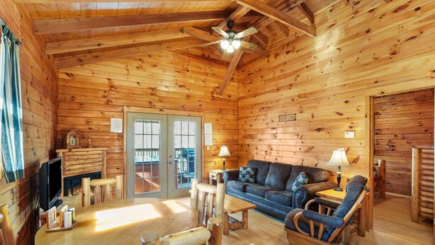 A log cabin interior with a wooden floor, a sofa, a table, and a television. - Sunset Ridge Cabin | 200 Acres, Pets, Hot Tub (South Bloomingville)