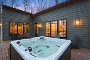 Un bain à remous sur une terrasse en bois, avec vue sur une maison et des arbres.