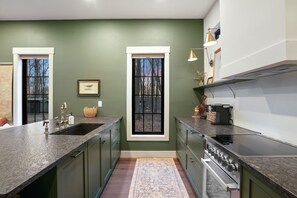 Une cuisine avec des murs verts, deux fenêtres, une cuisinière et un évier.