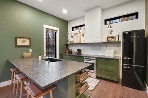 Una cocina moderna con gabinetes verdes, un refrigerador negro y una isla de granito con taburetes de bar.