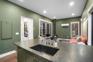 Una cocina con encimera de granito, un lavamanos y una estufa. Hay una ventana con persianas y una puerta que da a otra habitación.