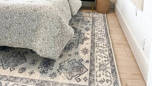 Makuuhuone, jossa on sänky, yöpöytä, lamppu, ruukussa oleva kasvi ja koristeellinen seinävaate.