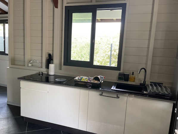 Een moderne keuken met een zwart aanrecht, witte kastjes, een raam met uitzicht op groen en een spoelbak met een kraan.