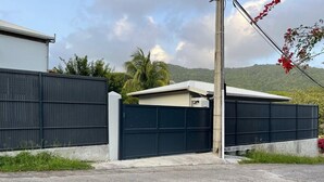 Una proprietà recintata con garage e un piccolo edificio, circondata da una recinzione metallica e vegetazione.