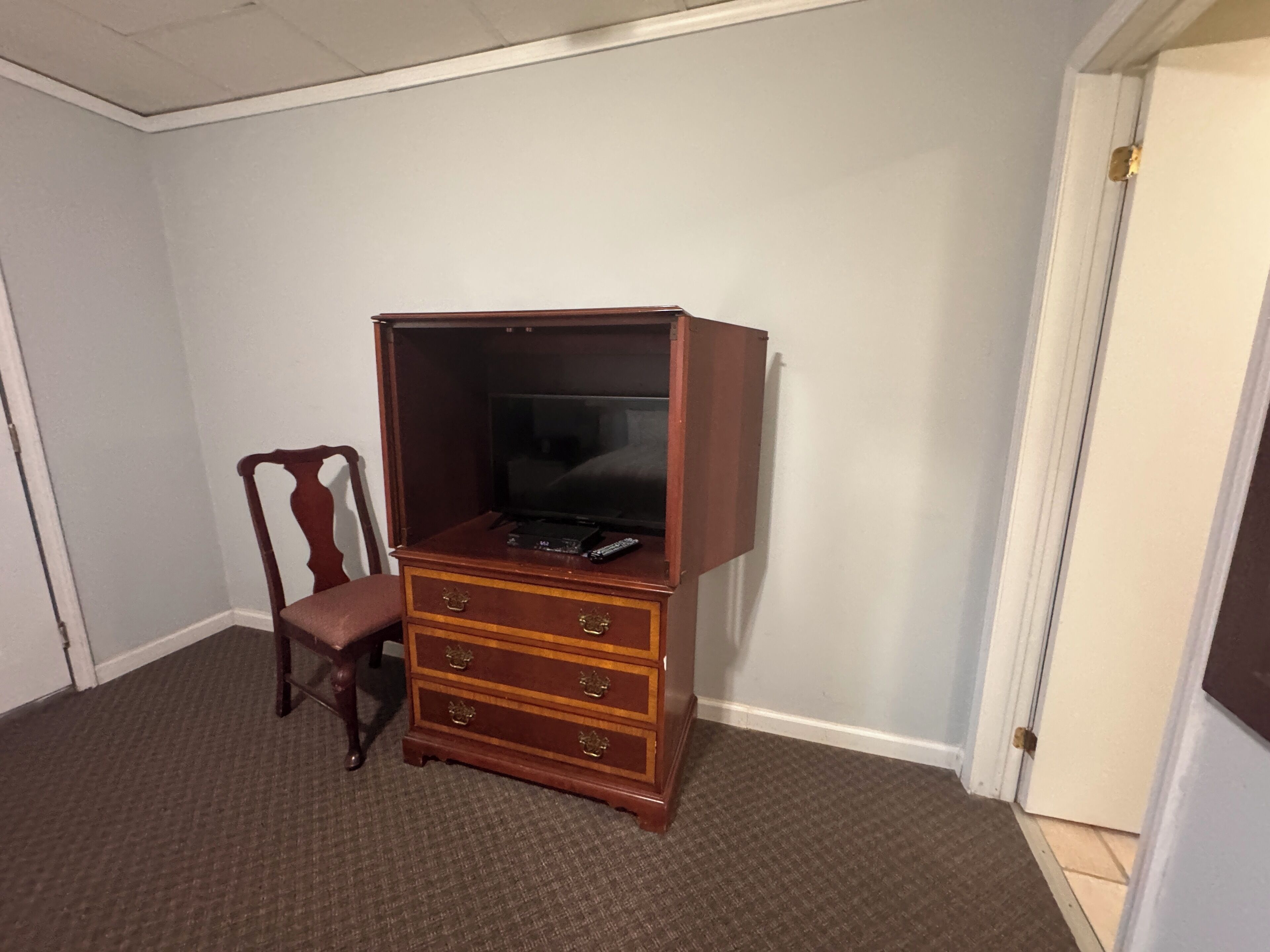 Una stanza con un armadietto in legno contenente una televisione, una sedia e una porta.