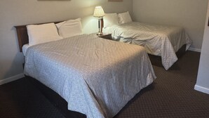 A hotel room with two beds, a nightstand, a lamp, and two framed pictures on the wall.