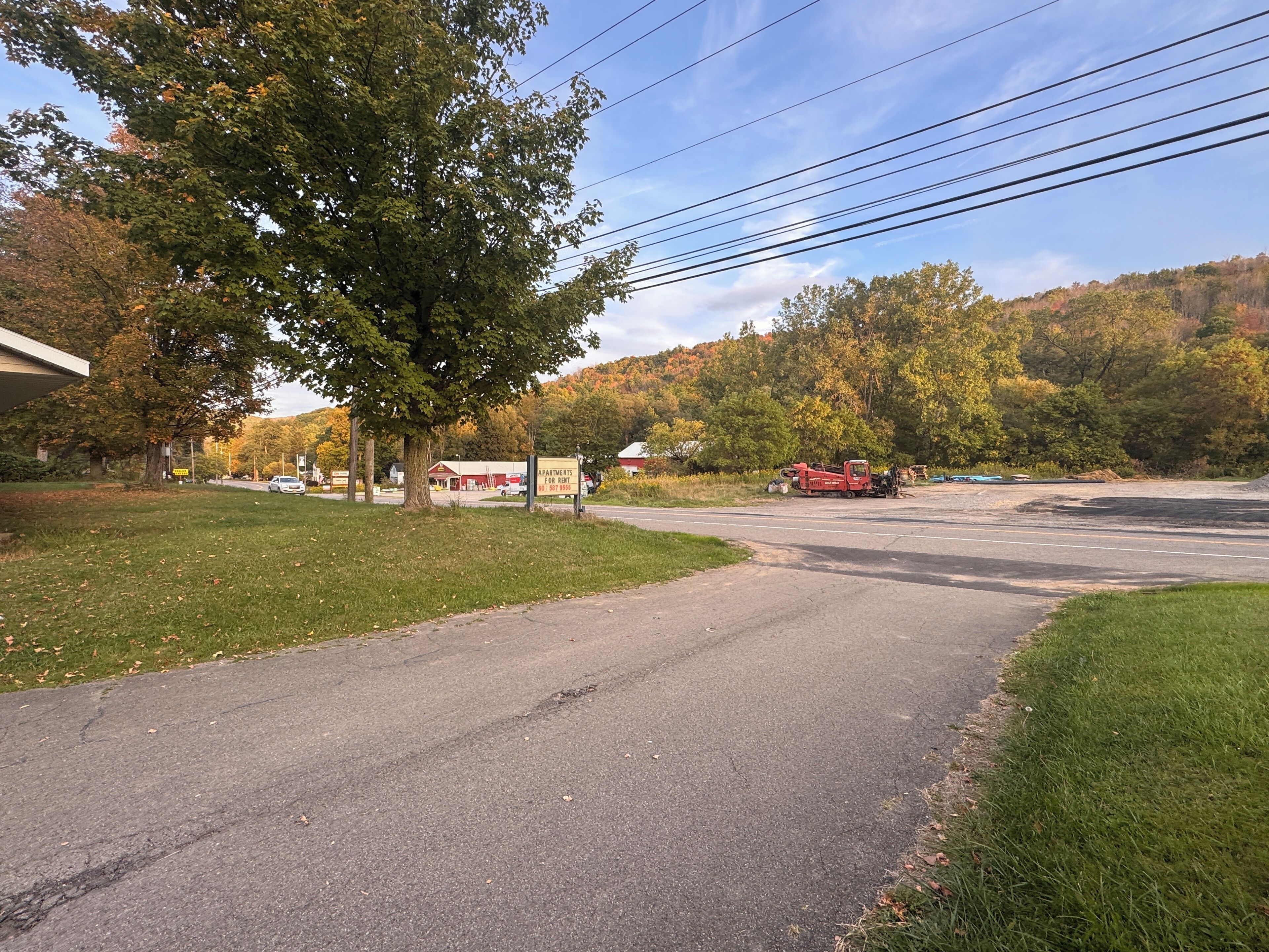 A road with a grassy median, a red truck, and a building with a 'For Rent' sign.