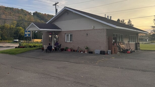 A small brick building with a porch, a sign indicating it's an inn, and a few potted plants around.