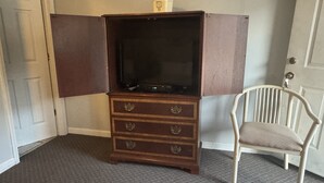 A room with a wooden cabinet containing drawers and a television. There is a white chair next to the cabinet.