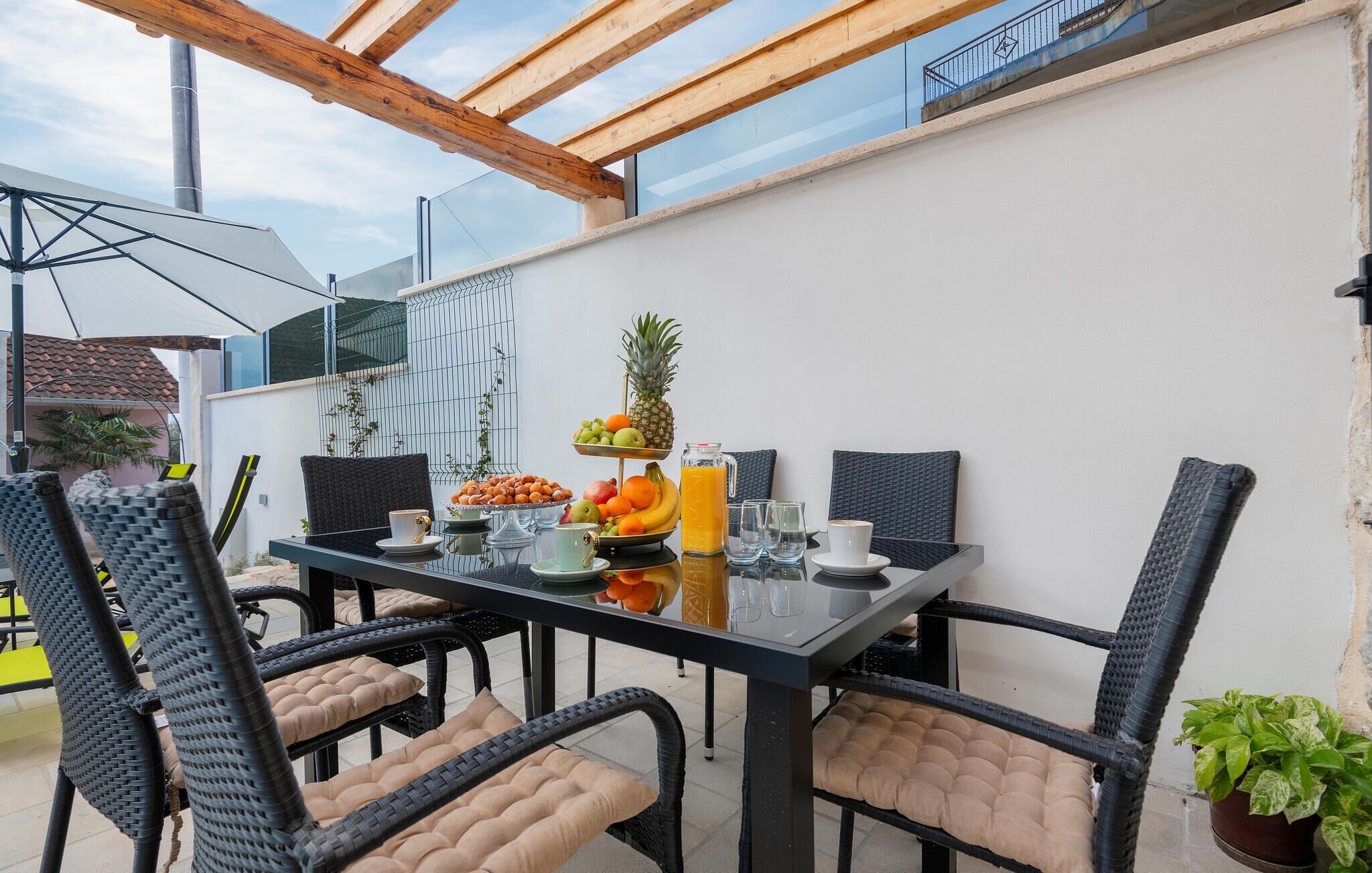Un espace de restauration en plein air avec une table en verre, des chaises en osier et une variété de fruits et de boissons.