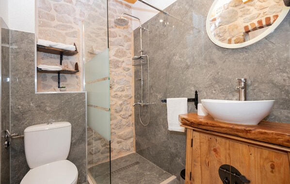 A modern bathroom with a stone wall, a glass shower enclosure, a wooden vanity, and a white sink. - Nice home in Vinjani Donji (Vinjani Donji)