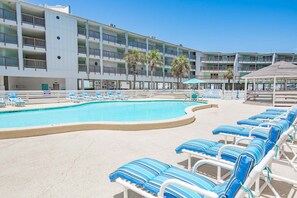 Un hotel con piscina, sillas de descanso y un edificio de varios pisos con balcones.