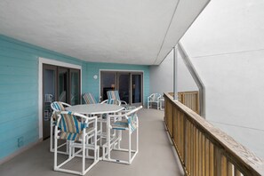 Un espacio exterior cubierto con una mesa y sillas blancas, barandilla de madera y pared turquesa.