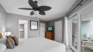 A bedroom with a bed, a ceiling fan, a dresser, a television, and a sliding glass door leading to a balcony with chairs. - La Mirage Condo 214 Beachfront Resort Condominiums with Private Boardwalk (Port Aransas)