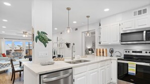 Una cucina moderna con mobili bianchi, elettrodomestici in acciaio inossidabile e illuminazione a sospensione.