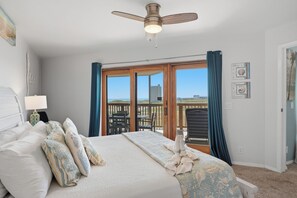 Une chambre dotée d’un grand lit, d’un ventilateur de plafond, d’une vue sur la plage et d’un balcon aménagé avec du mobilier d’extérieur.