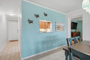 Una habitació amb una paret d'accent color turquesa, una taula de menjador de fusta i una cuina visible a través d'una finestra.