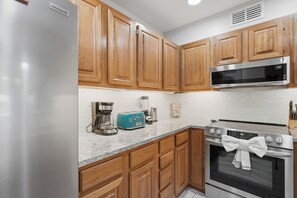 A kitchen with wooden cabinets, a stainless steel refrigerator, a microwave, a toaster, and an oven. - La Mirage Condo 323 Beachfront Resort Condominiums with Private Boardwalk (Port Aransas)