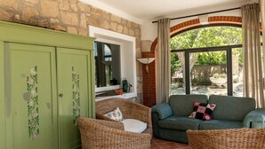 A cozy living area with wicker furniture, a green cabinet with floral designs, and a view of the garden through a large window. - Le Cascate by Interhome (Saturnia)