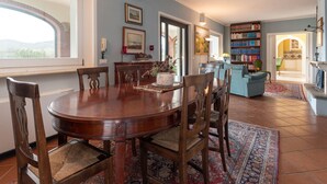 A dining area with a wooden table and chairs, a bookshelf, and a view of the outdoors. - Le Cascate by Interhome (Saturnia)