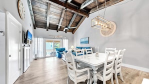 A dining area with a white table and chairs, a ceiling with exposed beams, and a view to the outside. - Pet Friendly! Private Beach Access! Chateau La Mer 8C Destin! (Destin)