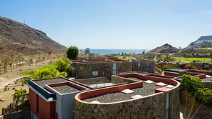 A rooftop with stone and red walls, a view of the ocean, and a hilly landscape in the background. - Spectacular house with private heated pool in paradise (Mogán)