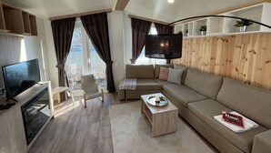 Una sala de estar moderna con un sofá, una mesa de centro, un televisor y un ventanal con cortinas.