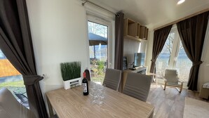 Un comedor moderno con una mesa de madera, sillas, una botella de vino y un televisor.