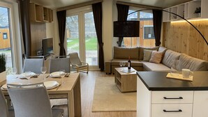 A modern living room with a dining area, a sofa set, a TV, and a large window with curtains. - Tiny Haus Altmühlpanorama by Interhome (Riedenburg)
