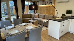 A modern, well-lit living area with a dining table set for two, a sofa, and a kitchen with white cabinets and a black countertop. - Tiny Haus Altmühlpanorama by Interhome (Riedenburg)