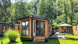 A small wooden cabin with a sliding glass door, surrounded by lush greenery and other cabins. - Tiny Haus Altmühlpanorama by Interhome (Riedenburg)