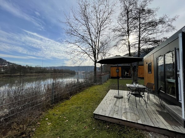 Eine moderne Terrasse im Freien mit Tisch und Stühlen, mit Blick auf einen Fluss und einen bewaldeten Bereich.