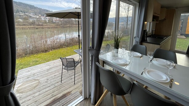 A dining area with a table set for two, overlooking a lake and a hilly landscape. - Tiny Haus Flussblick by Interhome (Riedenburg)