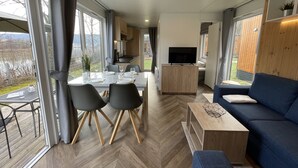 A modern living room with a sofa, a coffee table, and a dining area with a table set for four. - Tiny Haus Flussblick by Interhome (Riedenburg)