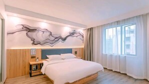 Une chambre d’hôtel moderne avec un grand lit, une tête de lit en bois, une table de chevet et une œuvre d’art abstraite accrochée au mur.