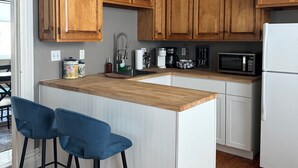Een moderne keuken met houten kasten, een wit kookeiland met barstoelen, een magnetron en een koelkast.