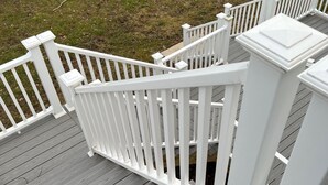 Een houten terras met witte leuningen en een gazon.