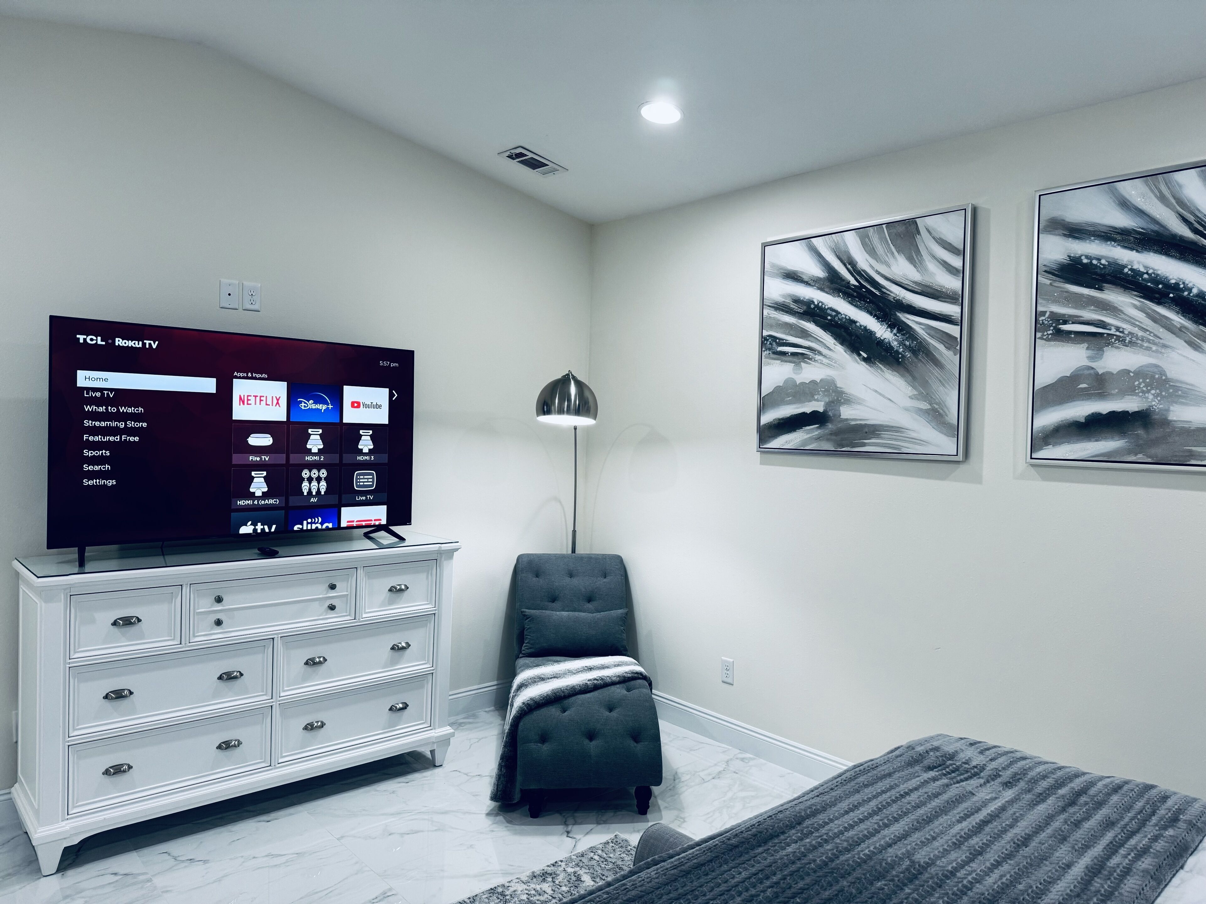 Ein modernes Wohnzimmer mit Flachbildfernseher, einer weißen Kommode, einem grauen Sofa und abstrakter Wandkunst.