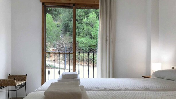Ein Schlafzimmer mit einem großen Bett, einem Sessel und einem Balkon mit Blick auf Bäume.