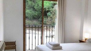 Ein Hotelzimmer mit zwei Betten, einem kleinen Sessel, einem Fenster mit Blick ins Grüne und einem Balkon mit Metallgeländer.